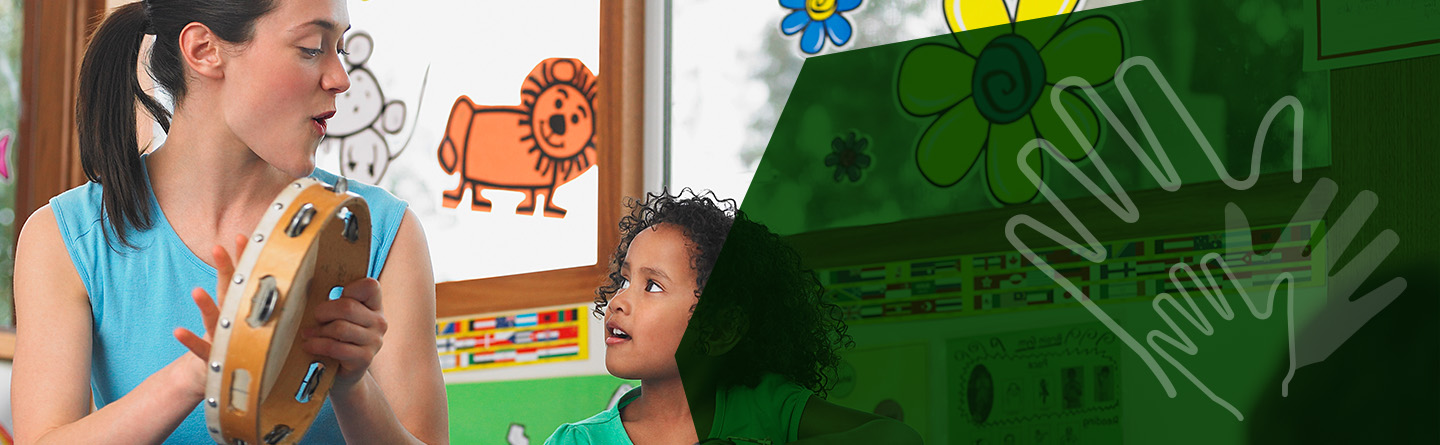 Header: Eine Erzieherin spielt in einem Kindergarten neben einem Kind Tamburin.